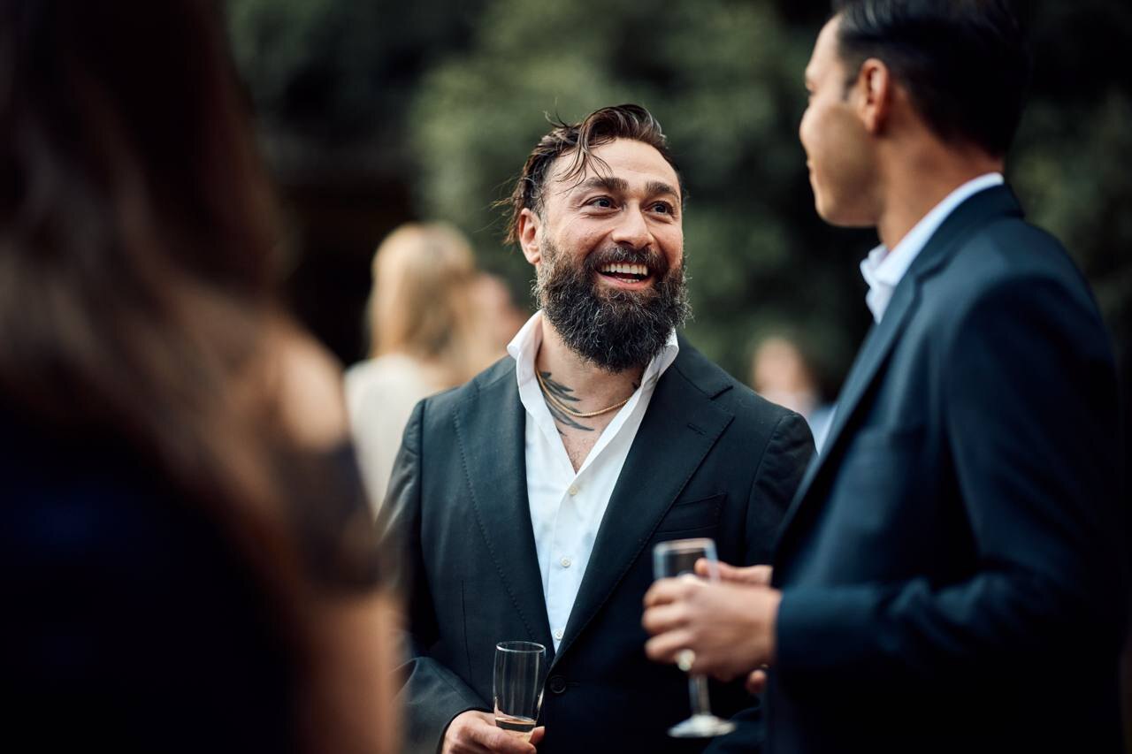 Emre Turan, laughing, in a dark jacket and open white shirt at an evening reception